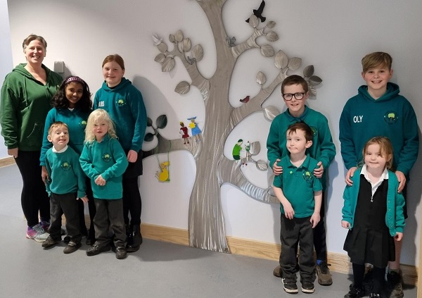 Head teacher Carol Bond with year 6 and Reception children alongside the artwork Our Elm Park Tree, designed and created by Somerset metalwork sculptor Ian Marlow.